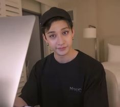 a young man sitting in front of a laptop computer while wearing a black shirt and cap