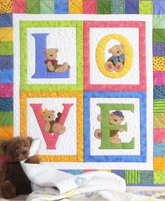 a teddy bear sitting in front of a quilted wall hanging with the word love on it