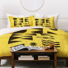 a bed with yellow comforter and pillows on top of it next to a coffee table