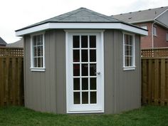 a small gray and white shed in the yard with sliding glass doors on it's side