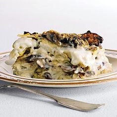 a white plate topped with lasagna covered in cheese and mushrooms next to a fork