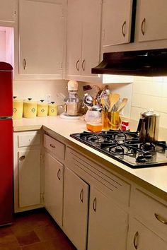 a red refrigerator in a white kitchen next to cabinets and counter tops with dishes on it