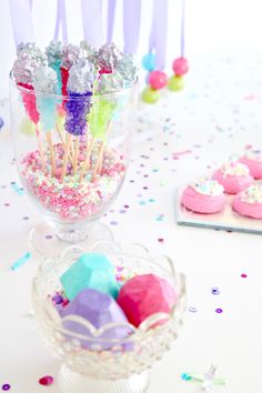 there are many colorful candies in the glass bowl on the table with confetti and sprinkles