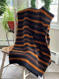 a black and orange blanket sitting on top of a chair next to a potted plant