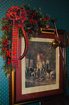 a christmas wreath is hanging on the wall above a framed photo with a hunting scene