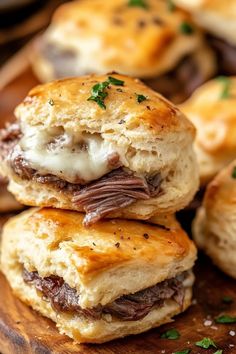 three biscuits stacked on top of each other with meat and cheese in the middle, sitting on a wooden cutting board