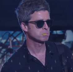 a man with sunglasses on his face wearing a black shirt and yellow sticker in his mouth