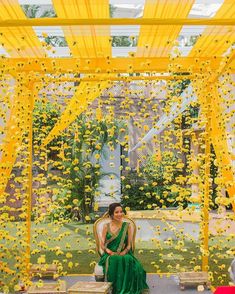 a woman sitting on top of a wooden bench under a yellow canopy covered in flowers