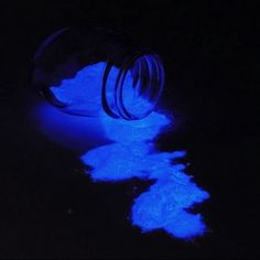 a bottle filled with blue fluorescent pigment sitting on top of a black table next to a glowing object