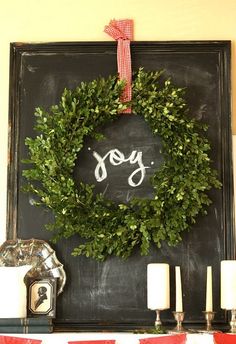 a chalkboard with the word joy written on it next to candles and a wreath