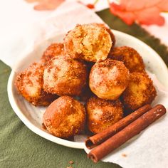 cinnamon sugar donuts on a white plate next to two cinnamon sticks and a napkin