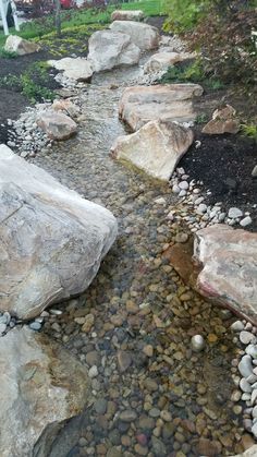 a stream running between two large rocks in the middle of a yard with grass and trees