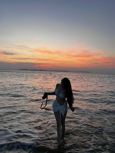 a woman standing in the water at sunset with her hair blowing back and holding an umbrella