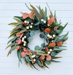 a wreath is hanging on the wall with leaves and berries around it, along with other greenery