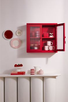 a red cabinet with plates and cups on it next to a white radiator