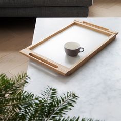 a coffee cup sitting on top of a white table next to a gray couch and wooden tray