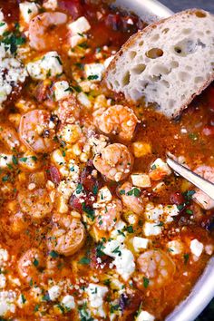 a bowl of greek shrimp soup with tomatoes and feta on the side, served with bread