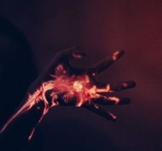 a person's hand with red and black paint on it, against a dark background