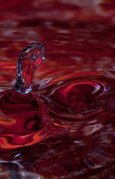 a red liquid droplet is seen in the water with ripples on it's surface