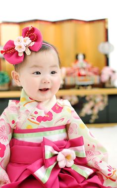 a baby girl wearing a pink and green kimono with flowers on it's head