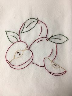 an embroidered piece of fruit with leaves and two apples on the side, sitting on a white towel