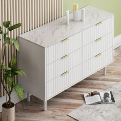 a white dresser with two candles on top and a magazine next to it in front of a green wall