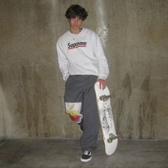 a young man holding a skateboard in front of a concrete wall with the word supreme on it