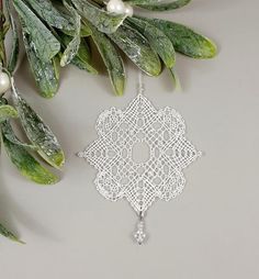 a white lace doily hanging from a tree branch with green leaves and flowers in the background