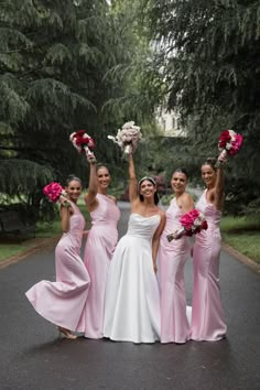 four bridesmaids in pink dresses holding bouquets and posing for the camera on a paved road