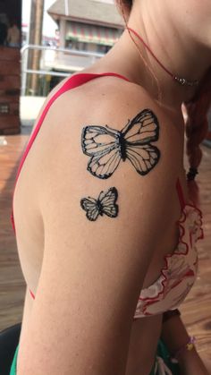 a woman's shoulder with two butterflies tattooed on the back of her left arm