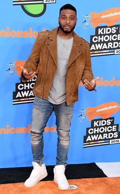 a man standing on top of an orange carpet in front of a blue wall with the words kids'choice awards written on it