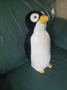 a stuffed penguin sitting on top of a green leather couch next to a black and white pillow