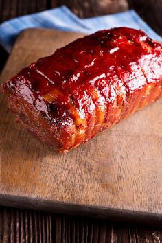 a piece of meat covered in ketchup sitting on top of a wooden cutting board