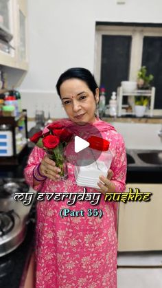 a woman in a pink dress is holding flowers and smiling at the camera while standing in a kitchen