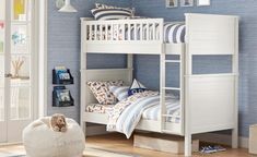 a white bunk bed sitting next to a window in a room with blue walls and wooden floors