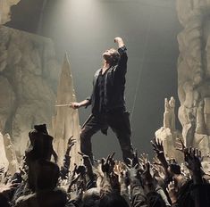 a man standing on top of a stage with his arms in the air and hands raised