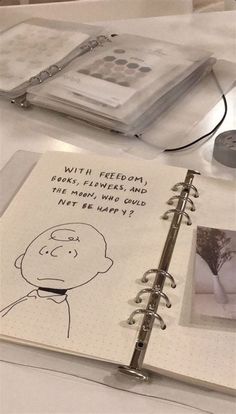 an open notebook on a table with pictures and words written in it, along with a pen