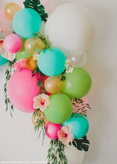 balloons and greenery are arranged in the shape of a flower arrangement on a white wall