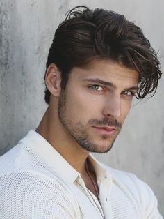 a close up of a person wearing a white shirt and posing for a photo in front of a concrete wall