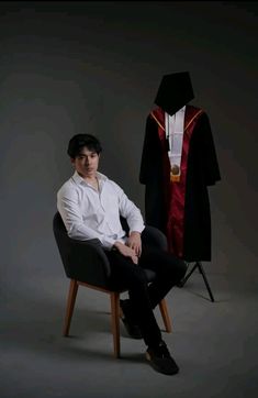 a young man sitting in a chair next to a robe on a mannequin