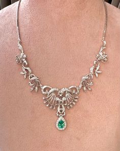 a woman wearing a necklace with an emerald stone in the center and silver filigrees on it