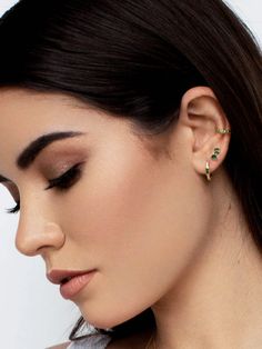 a woman wearing an earring with green stones on the back of her ear, looking down