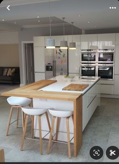 a kitchen with an island and three stools in front of the counter top that has two ovens on it