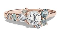 three stone engagement ring in rose gold with blue and white diamonds on the band,