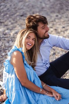 a man sitting next to a woman on the beach smiling at each other's eyes