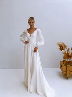 a woman wearing a white dress standing in front of a wooden box with dried plants