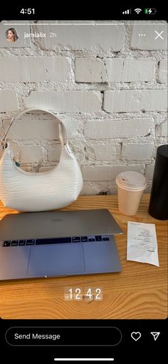 an open laptop computer sitting on top of a wooden table next to a white purse