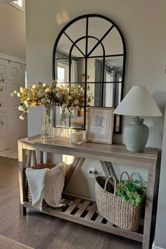 a table with baskets and vases on it in front of a mirror, lamp and door