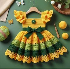 a crocheted dress with green and yellow trims on a hanger next to balls of yarn