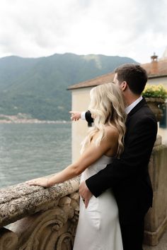 a bride and groom standing on a balcony overlooking the water